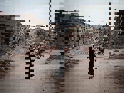 Woman dressed in black, walking through a street in Syria surrounded by rubble from destroyed buildings